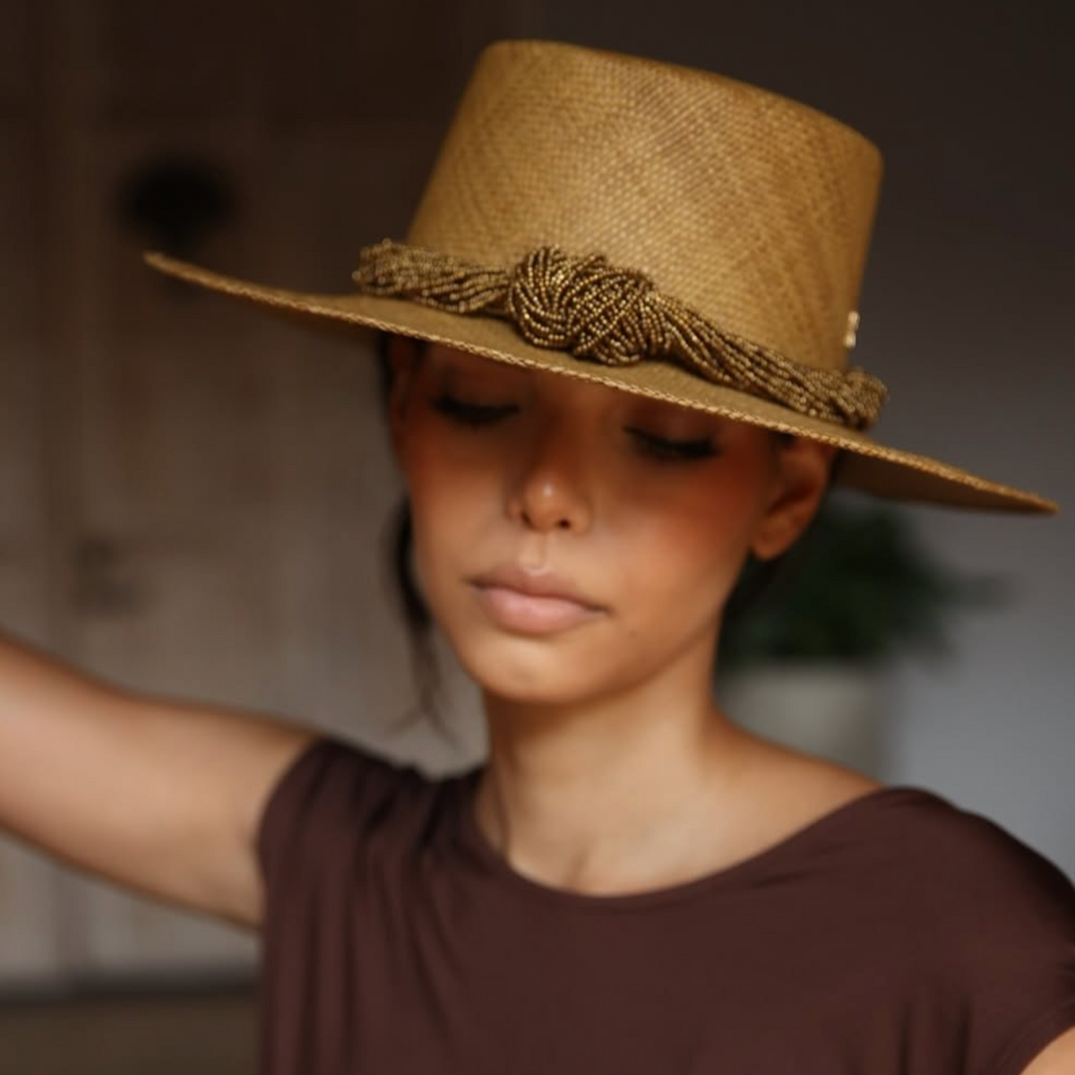Woman wearing a brown straw hat with decorative band against a neutral background