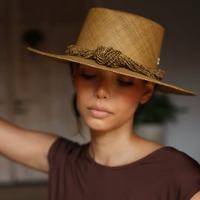 Woman wearing a brown straw hat with decorative band against a neutral background