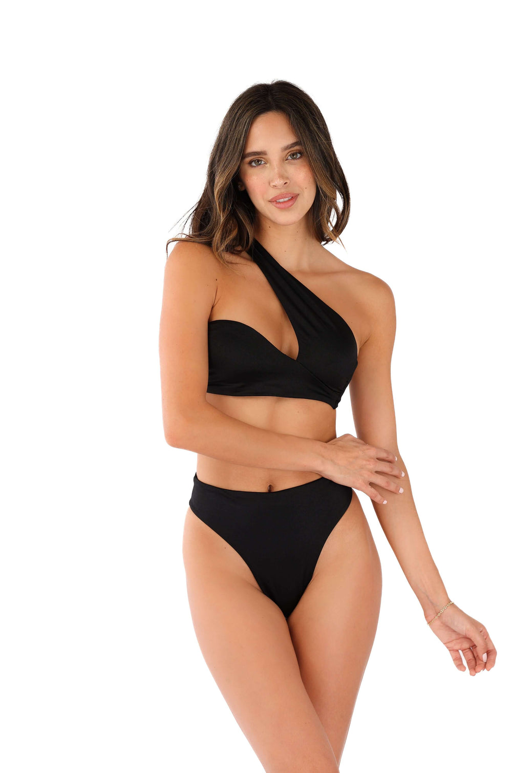 A person poses against a white background, wearing the Sofia One Shoulder Bikini Top in black, which features an asymmetrical design. Their confident gaze at the camera and one arm resting on their waist add to its unmistakable high-fashion edge.