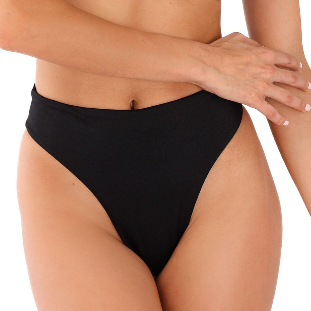 A person stands against a plain background, showcasing their style in the Sofia High Waisted Bikini Bottom in black. One arm rests gracefully across their midriff, enhancing the elegant look of the high-cut design.