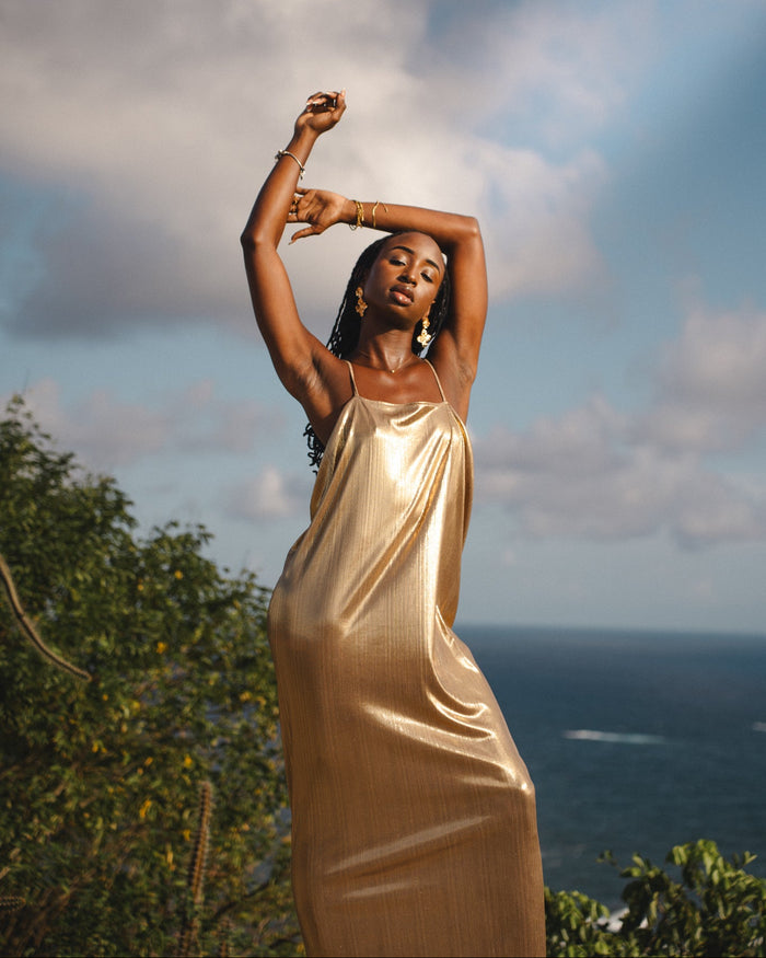 Woman in a gold dress standing outdoors with ocean and sky in the background