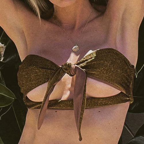 A person wears the textured brown Frankie Bikini Top with a central knot and pendant necklace, set against lush greenery that highlights the glistening fabric.