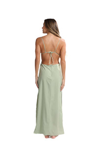 A person adorned in the Katt Clip On Maxi Skirt stands barefoot, facing away. Their long hair cascades down their back, enhancing the minimalist elegance. The versatile tied design near the shoulder blades flows beautifully to the ankles against a white background.