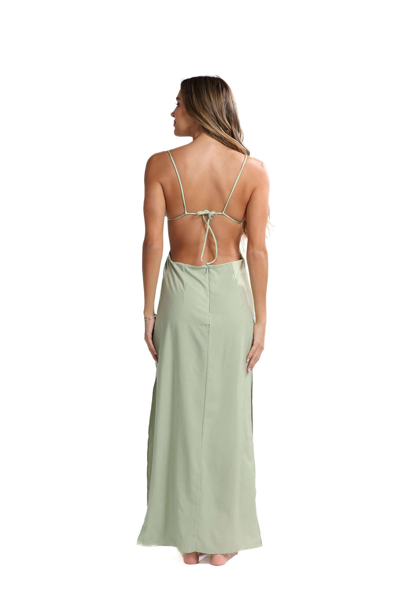 A person adorned in the Katt Clip On Maxi Skirt stands barefoot, facing away. Their long hair cascades down their back, enhancing the minimalist elegance. The versatile tied design near the shoulder blades flows beautifully to the ankles against a white background.