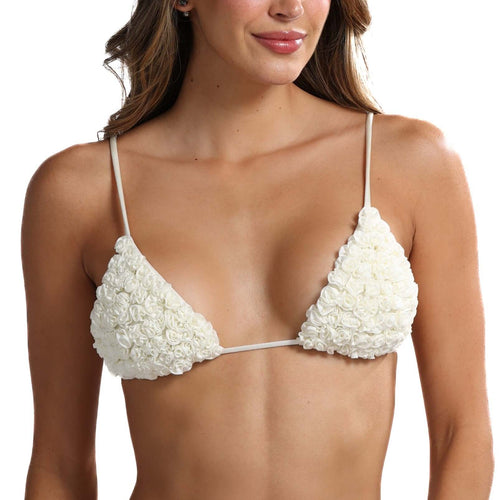 A woman presents the Katt Triangle Bikini Top from our latest swimwear collection. This white bikini is highlighted by floral-textured cups embellished with handcrafted mini rosettes and complemented by thin straps. Her long brown hair flows gracefully as she smiles softly against a simple white backdrop.