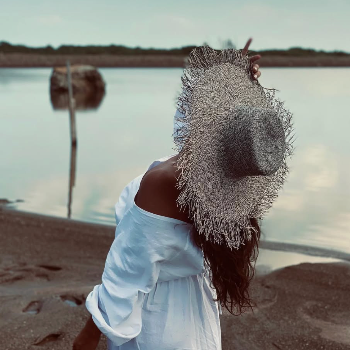 Woman on a beach wearing a straw hat and white dress with a blurred background