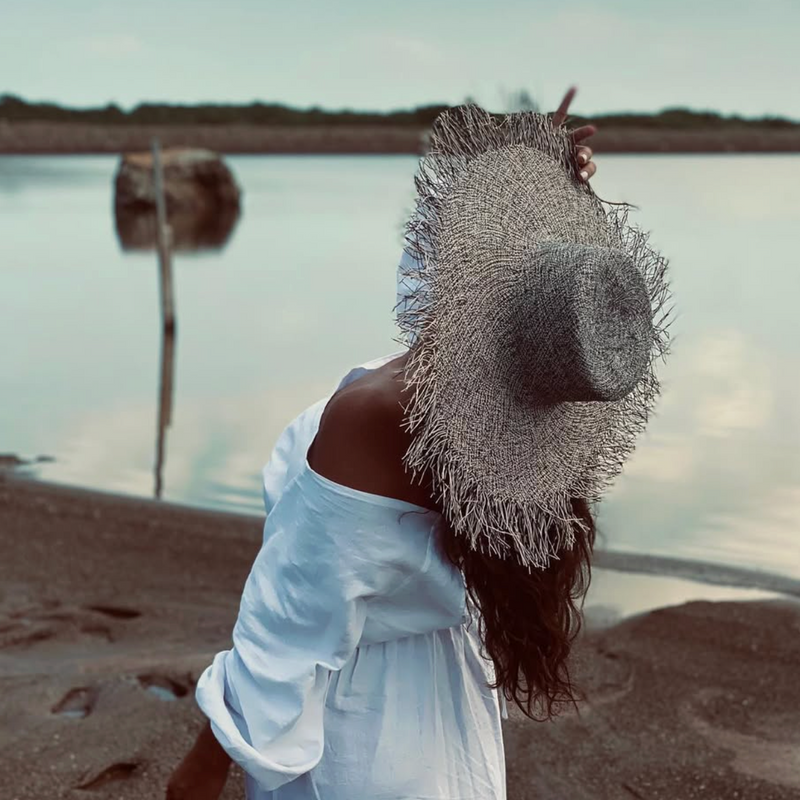 Woman on a beach wearing a straw hat and white dress with a blurred background